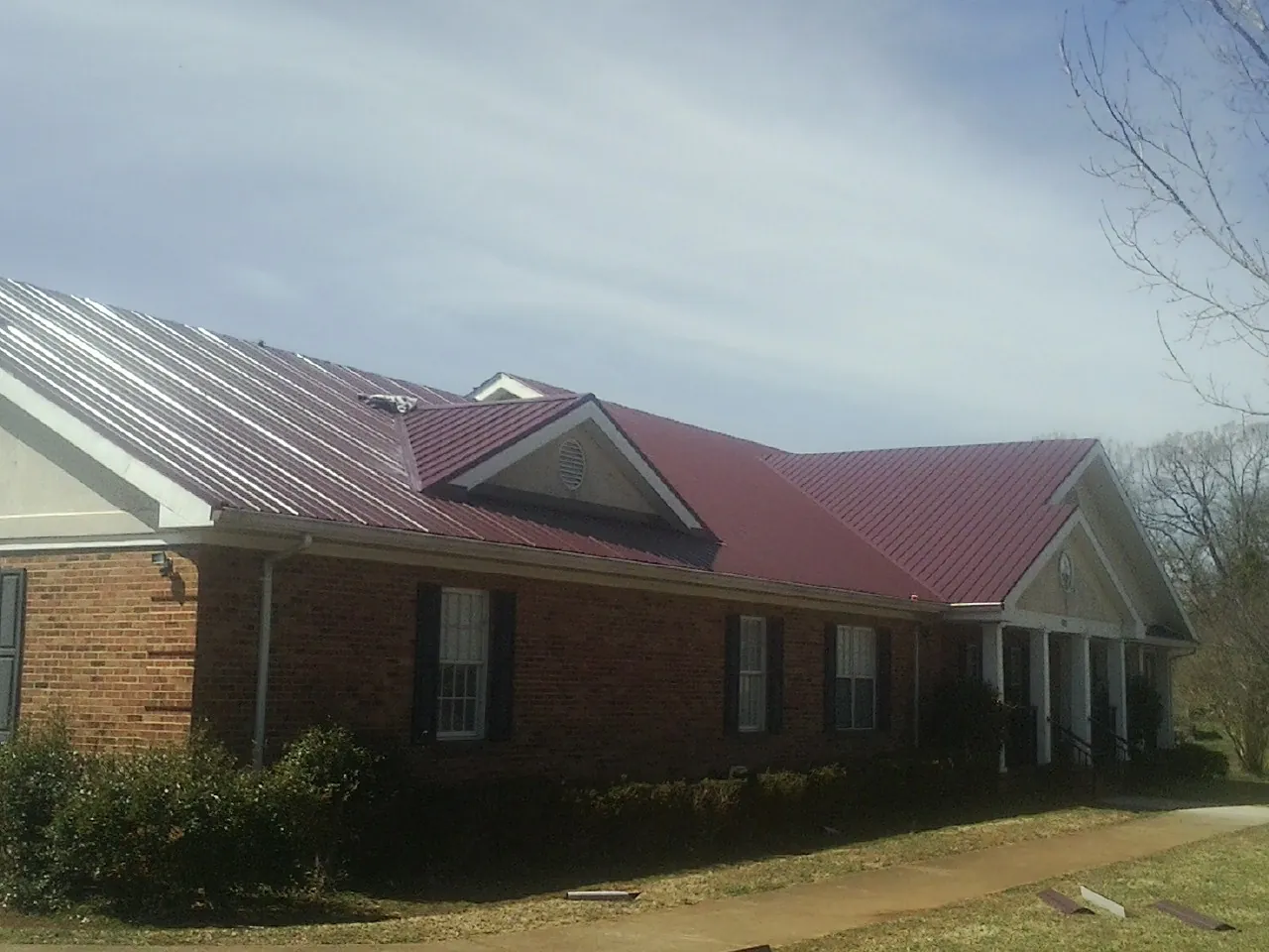 Red metal roof with gabled entries on a long brick building, from a Hail Damage Roof Repair job in Redding