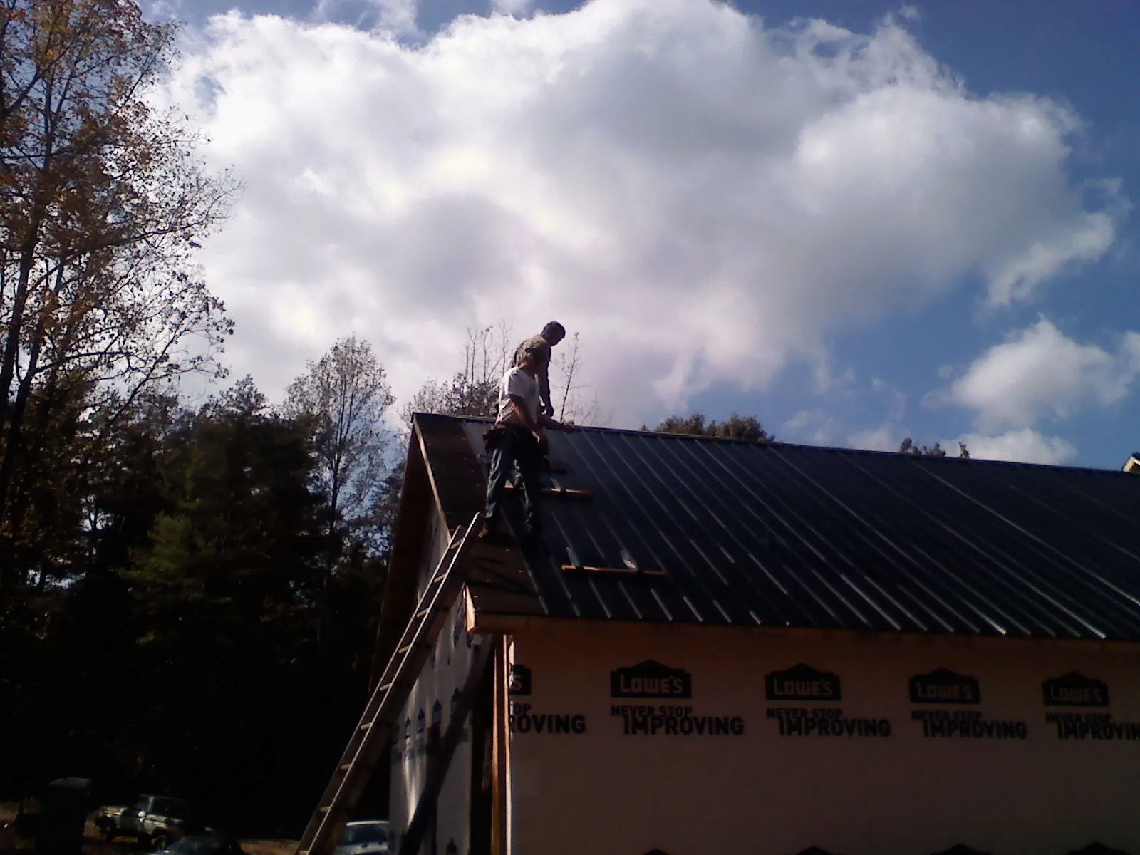 Roofer fastening dark metal panels high against a cloudy sky, from a Roof Inspection job in Redding